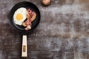 Traditional English breakfast with fried eggs and bacon in cast iron pan on dark concrete...