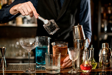 Bartenders hand holds tongs with large square piece of ice
