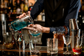 barman gently pours blue cocktail from mixing cup into glass