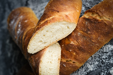 Traditional french baguette with flour on a dark background close-up.