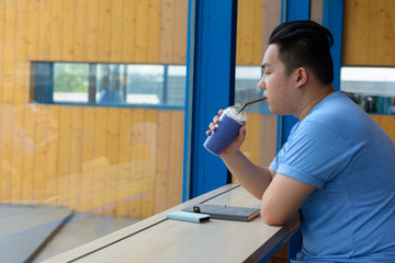 Fototapeta premium Young overweight Asian man drinking coffee at the coffee shop