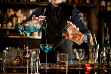 young bartender professionally pours cocktails into glasses.