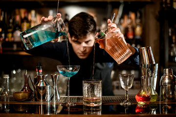 young bartender professionally pours cocktails into glasses and looks at it.