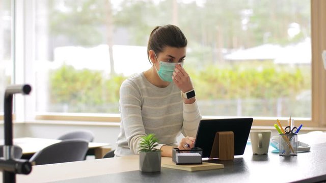 remote job, business and health concept - young woman in face protective medical mask with tablet pc computer and notebook working at home office