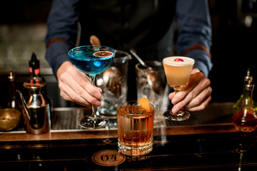 Close-up. Male bartender presents three different cocktails