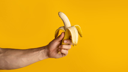 Closeup of guy holding half peeled banana on orange background, blank space. Panorama