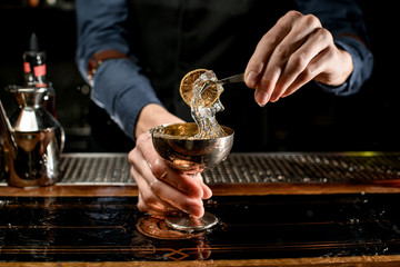 bartender holds beautiful metal glass and decorate it with slice of citrus