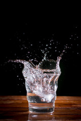 Water splash with transparent glass on wooden table with black background. Copy space for your text.