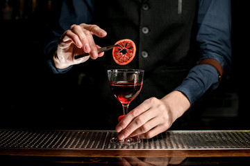 bartender decorates transparent glass with slice of citrus