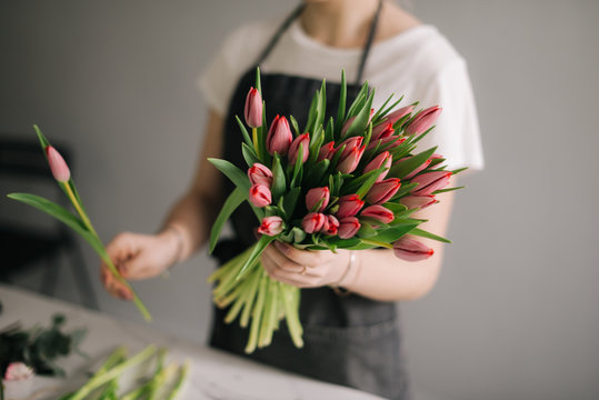 Unrecognizable young woman florist wearing apron making floral composition from fresh roses at the table on white background. Concept of working with flowers, floral business.