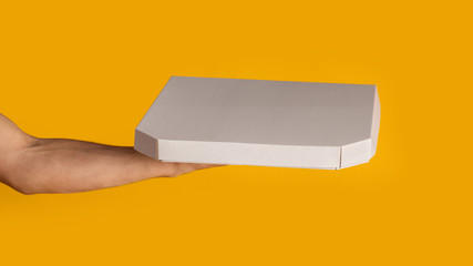Unrecognizable delivery man holding box with takeaway pizza on orange background, mockup for design. Panorama