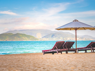 Chairs and umbrella on the beach near ocean. Winter vacation in hot places. Sunshine and moody sky