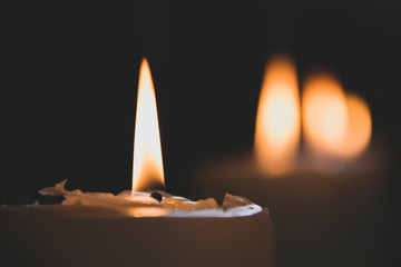 Close up of classic candle with orange flames burning on wax with bokey of other candles in church