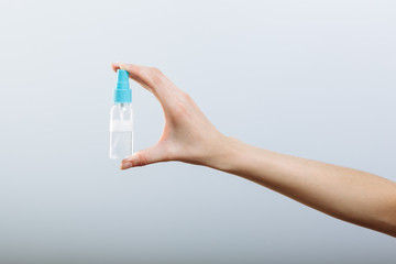 Woman's hand holding spray bottle sanitizer isolated on gray background