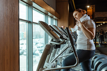 tired overweight girl touching towel while working out on stepper