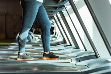 Fototapeta na wymiar cropped view of overweight girl in leggings running on treadmill in gym