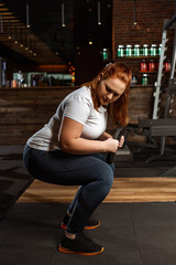 concentrated overweight girl squatting with weight disc in gym