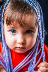 A little girl on a black background with Afro-pigtails, artificial plaited in elastic bands and put on