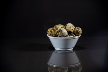 Quail eggs in a white pot scattered on a mirrored background