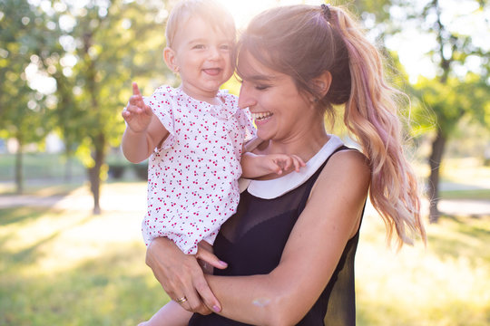 Horizontal Portrait Against A Nature Background Of A Cheerful Twenty Five Year Old Woman With One Year Old Daughter In Her Arms