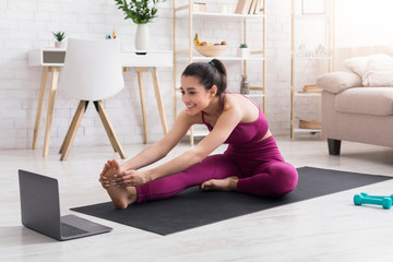Self isolation workout. Joyful girl in sportswear practicing yoga or stretching with online...