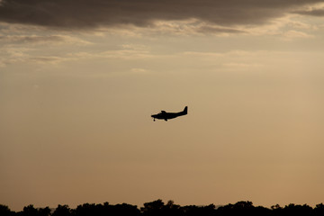 Fototapeta na wymiar silhouette of small airplane landing in sunset with clouds 