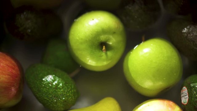 Overhead dolly of apples, avocados and mangos floating in a kitchen sink
