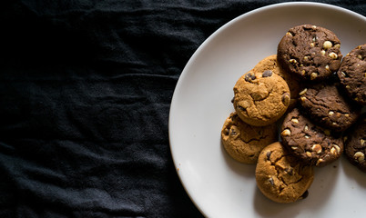 Flat lay. Freshly baked double black and white  chocolate chip cookies on a white plate and dark background, copy paste, recipe, culinary