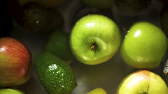 Slow dolly right of top-down view of apples and avocados floating in a kitchen sink