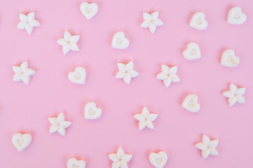 Top view on sugar in the shape of heart and flower on a pink background.