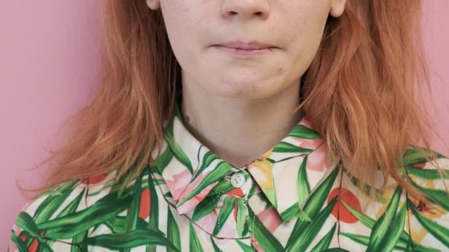 closeup on red headed girl in flowered shirt showing her tongue with colorful letters on it. weird gonzo crazy portrait of laughing and smiling unrecognisable young female on pink background