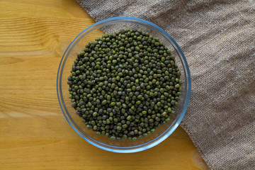 green mung beans in a glass bowl on yellow wooden table with sackcloth. top view. Healthy lifestyle.