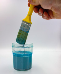 paintbrush dipped into vivid blue paint in glass jar
