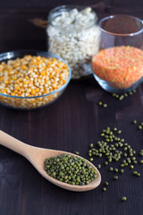 Healthy lifestyle. green mung beans with wooden spoon on a black background.  different kinds of groats: yellow corn, white beans and green mung in jars on a wooden table.