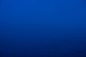 Obraz premium Natural texture of deep blue calm water in dusk close up. Night sea of blue classic color. Water ripple nature background. Meditative image of thick fog above lake. Soft light shines on water surface.