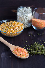 red and yellow lentils, corn, white beans and green mung on a black background. wooden spoon with lentils. different kinds of groats in bowls and jars on a wooden table. Healthy lifestyle.
