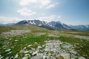 Atmospheric alpine landscape with stony meadow with green grass and big mountain ridges. Wonderful snowy mountains under blue sky. Idyllic place in highlands. Majestic scenery on high altitude.