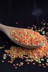 Healthy lifestyle. close-up red and yellow lentils in a wooden spoon on a black background. copy space. wooden spoon with dried red and yellow lentils on a wooden table.