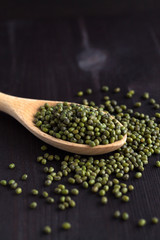 green mung beans in spoon on a black background. copy space. Healthy lifestyle. wooden spoon with dried mung beans on a wooden table. vertical