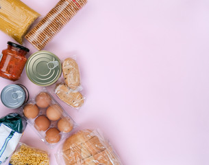 Top view on grocery set with pasta, canned food, eggs, bread, cookies. Food supplies, crisis food stock on pink background, copy space. Food layout. Quarantine, isolation period. Safe home delivery.