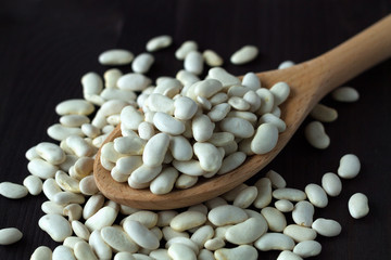 close-up white beans in spoon. Healthy lifestyle. wooden spoon with dried white beans on a wooden table. white beans in spoon on a black background. copy space. 