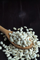 wooden spoon with dried white beans on a wooden table. Healthy lifestyle. white beans in spoon on a black background. copy space. vertical
