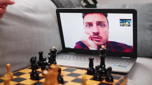 Two young men play chess at home in quarantine in isolation using a video call.