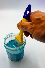 paintbrush dipped into vivid blue paint in glass jar