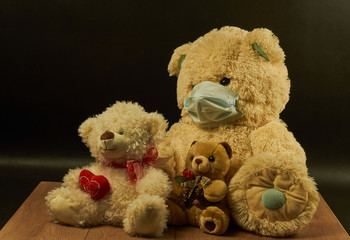 three soft toys of bears of different sizes, one in a medical mask on a black background