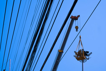 Low angle view of electrician on crane repairing electrical system of spotlight tower with many power lines against blue sky background
