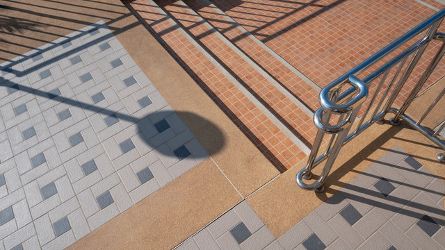 Sunlight and shadow on tile floor pattern surface of small staircase on different levels with stainless steel railing in exterior architecture concept, high angle view with copy space