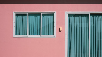 Sunlight on surface of glass sliding door and window with green curtains and doorbell on pink cement wall background, home exterior architecture concept