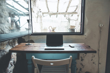 Home office desk made of recycled wood set up in a country house for smart working, with a view on the outside hills from the window. Quarantine and lockdown mood.