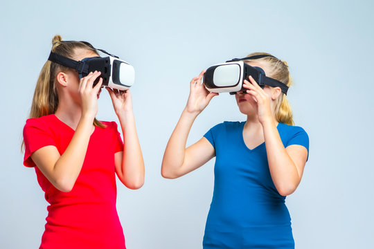 Virtual Reality Simulation. Pair of Caucasian Twin Teenager Girls Playing With VR (Virtual Reality) Helmets Together Indoors.